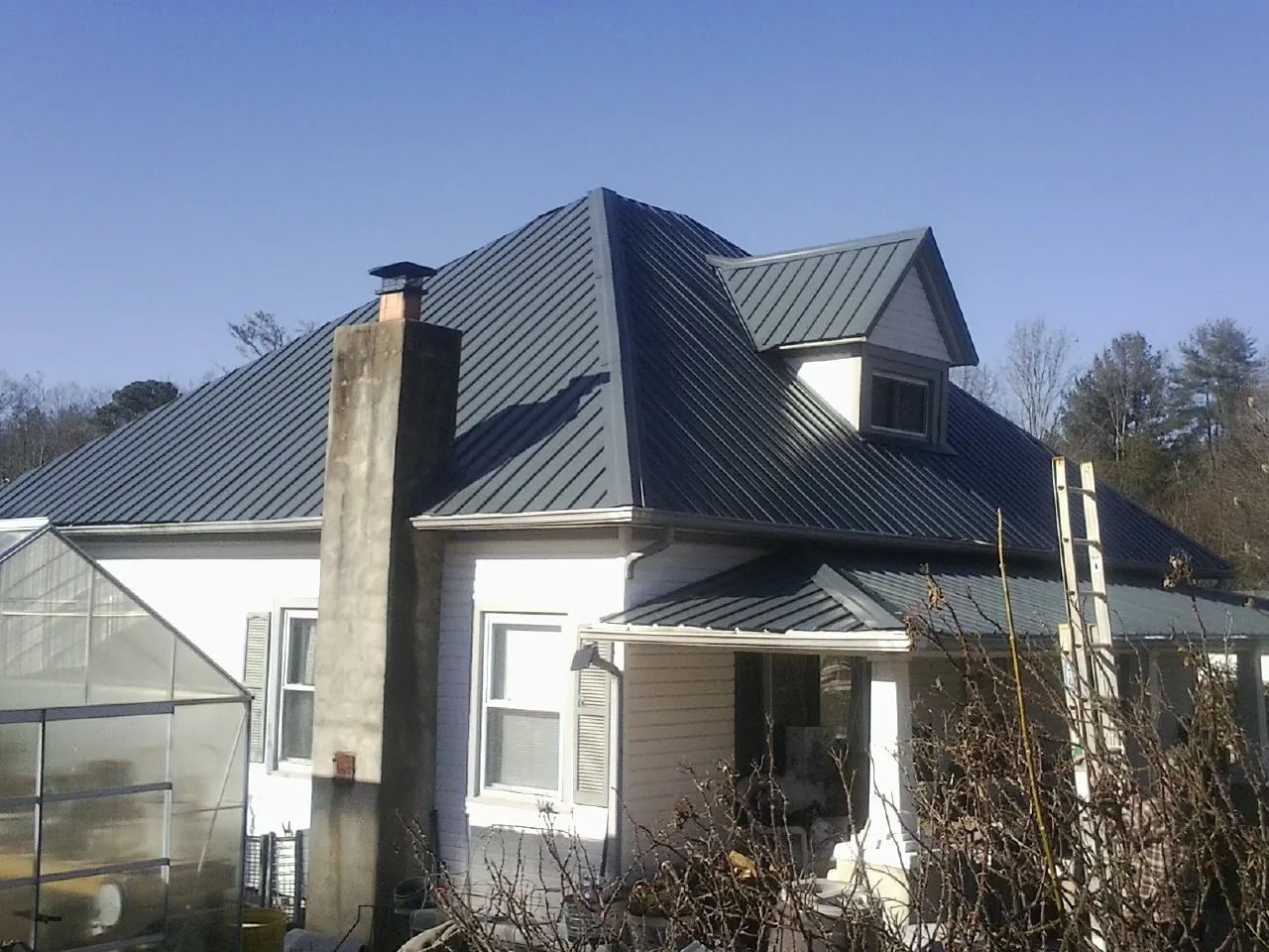 Dark blue standing seam metal roof on a white farmhouse with dormer — Slate & Tile Roof Repair by Roofing Brothers in East Kingston