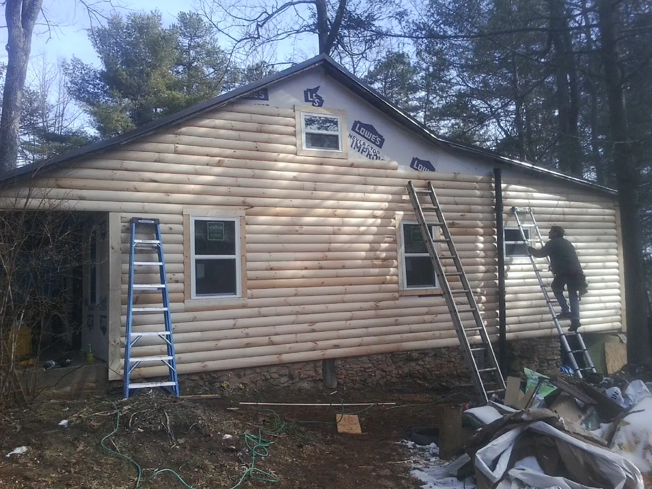 Ladders set against fresh log siding during an exterior remodel in East Kingston