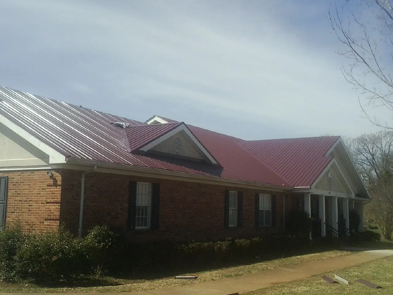 Red metal roof with gabled entries on a long brick building, from a Hail Damage Roof Repair job in East Kingston