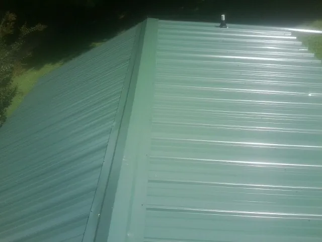 New green metal panels meeting at the ridge of a roof — Flat Roof Repair work by our crew in East Kingston