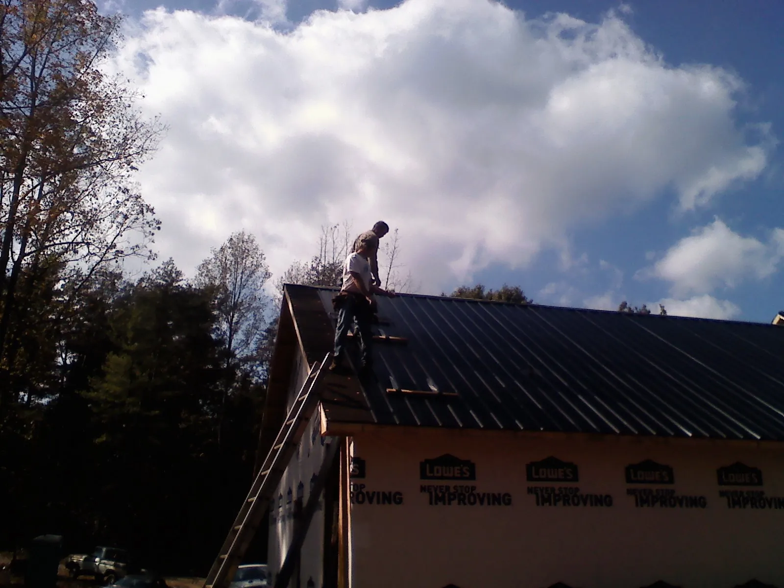 Roofer fastening dark metal panels high against a cloudy sky, from a Roof Inspection job in East Kingston