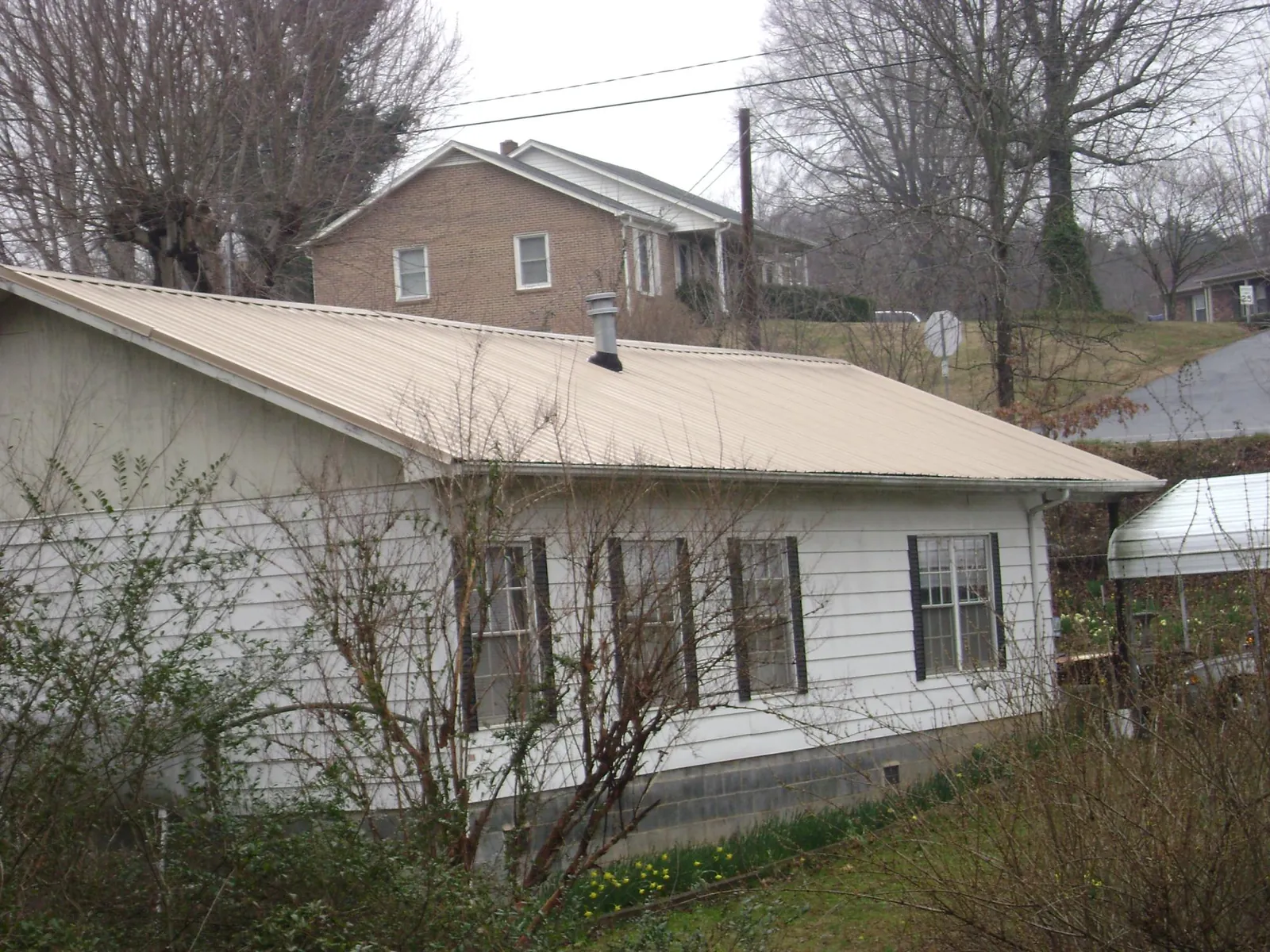 Tan metal roof on a white sided house set into a hillside — Commercial Roofing by Roofing Brothers in East Kingston