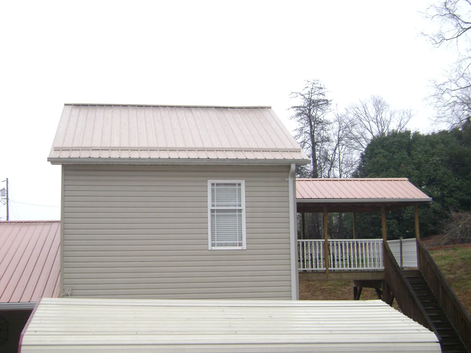 Tan metal roofs on a two story addition and attached porch, from a Roof Replacement job in East Kingston